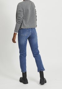 Gray textured sweater, blue denim jeans with a slim fit, and black ankle boots. The outfit is casual, with noticeable stitching on jeans.