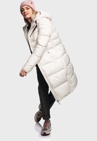 Lange witte pufferjas met een capuchon, voorzien van een gequiltte textuur en ritszakken, gecombineerd met zwarte broeken en multifunctionele sneakers in verschillende kleuren.