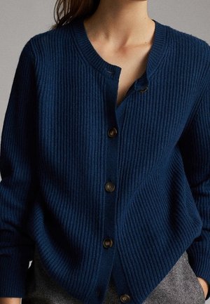 Navy ribbed cardigan with a rounded neckline, featuring a row of brown buttons and a loose fit, crafted from soft textured fabric.