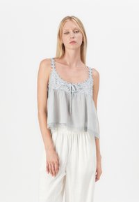 Lichtgrijze cropped top met kantdetails, ronde halslijn en een strik aan de voorkant. Gepaarde met witte, losse broek.