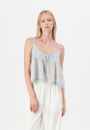 Top gris clair court avec des détails en dentelle, encolure ronde et un nœud au centre devant. Accompagné d'un pantalon blanc ample.
