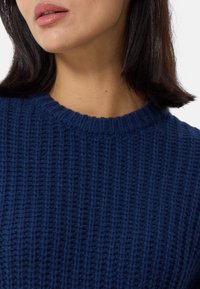 Maglione lavorato a maglia blu navy con coste testurizzate, caratterizzato da un colletto rotondo. Il tessuto appare morbido e spesso con dettagli di cucitura visibili.