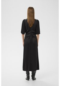 Musta satiininen maximekko, jossa on lyhyet hihat, vartalonmyötäinen yläosa ja hieman liehuva helma, yhdistetty mustiin korkeisiin saappaisiin.