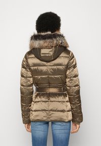 Chaqueta acolchada de color verde oliva con capucha con borde de piel, cinturilla ajustada y textura de colcha, que presenta un acabado brillante y un diseño ligero.