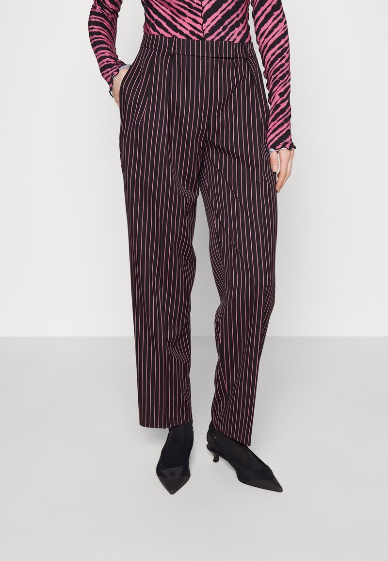 Personne portant un pantalon noir à rayures verticales roses, un haut rose et noir à imprimé zèbre, et des chaussures noires pointues à talons bas.