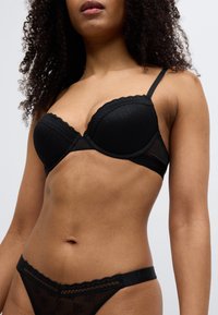 Μαύρο σουτιέν με δαντέλα στο τελείωμα και μπανέλα, με  σχέδιο στο ύφασμα. Συνδυάζεται με διαφανές μαύρο στρινγκ με δαντελένια άκρα που ταιριάζουν.