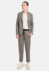 Blazer à carreaux avec un col à revers, associé à un pantalon ajusté avec cordon de serrage. Porté sur un haut beige clair. Bottines crème.