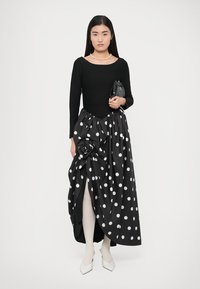 Black long-sleeve top paired with a polka dot skirt featuring a floral accent. The skirt drapes elegantly, revealing white tights and pointed shoes.