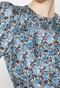 Gros plan d'un tissu avec un motif floral bleu et noir sur fond blanc, comprenant de petites fleurs regroupées et des feuilles foncées.