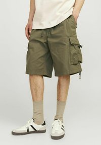 Oliwkowe szorty cargo z bocznymi kieszeniami, regulowanym sznurkiem w talii i długości do kolan, sparowane z białymi butami i beżowymi skarpetami.