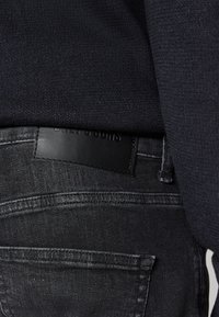 Jeans de mezclilla gris oscuro con una cinturilla texturizada, que cuentan con una parche de cuero negro grabado con "Only & Sons" en la parte trasera.