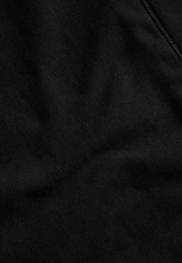 Svart tyg med en slät yta och lätt lyster, med subtila veck och en ren kantstickning längs ena sidan.