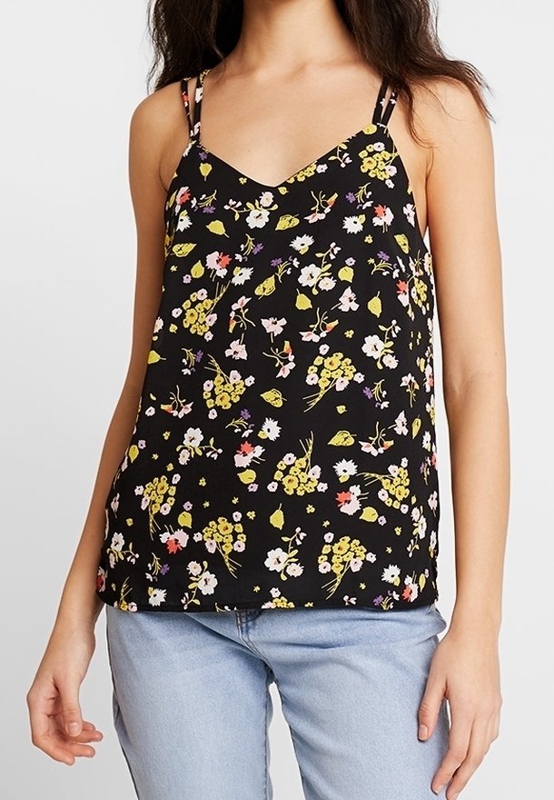 Femme portant un top noir fleuri sans manches à col en V avec de fines bretelles doubles et un jean bleu clair.