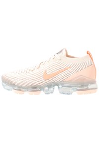 Scarpe da ginnastica beige chiaro con tomaia strutturata, dettagli rosa e ammortizzazione ad aria trasparente sulla suola. Presentano un logo Nike.