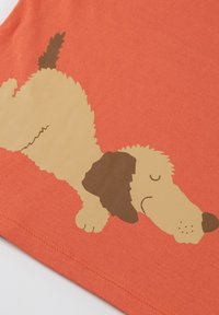 Orange cotton t-shirt featuring a printed cartoon dog with a beige body, black ear, and brown accents, lying down on the fabric.