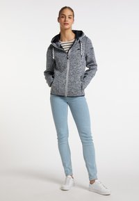 Felpa zip con cappuccio foderato in navy melange, con lacci e tasche laterali, abbinata a jeans skinny blu chiaro e sneakers bianche.