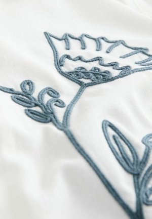 Embroidered floral design in blue thread on a white fabric background, featuring intricate leaf and petal shapes with textured detailing.