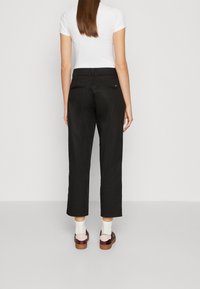 Czarne, krótkie spodnie o gładkiej fakturze, z paskiem i dwoma tylnymi kieszeniami na suwak. Noszone z białą koszulą i wielokolorowymi butami.