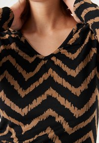 Black and tan zigzag patterned long-sleeve top with a V-neckline, made from soft, stretchable fabric.