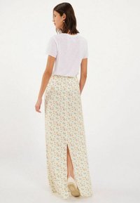 Jupe maxi fleurie en tissu léger, avec une fente sur un côté, présentant une base crème et des motifs de fleurs multicolores. T-shirt blanc uni porté.