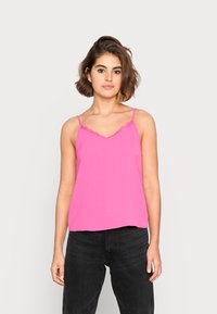 Top de alças rosa com rendas, feito de tecido suave, combinado com jeans pretos de cintura alta.