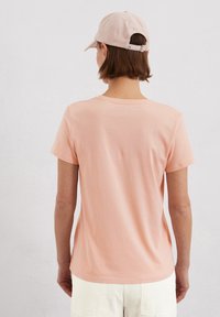 Jasnoróżowy bawełniany t-shirt z krótkim rękawem i okrągłym dekoltem, charakteryzujący się gładką fakturą i luźnym krojem. Widok z tyłu ukazuje prostotę.