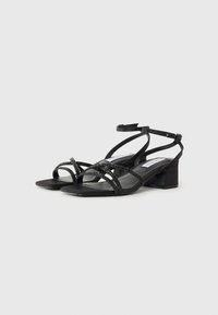 Sandales à talons carrés noires avec un design à lanières et des accents scintillants, finition lisse et bride de cheville ajustable. Forme de bout carré.