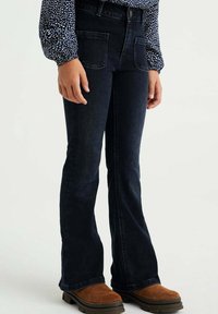 Mörkblå utsvängda jeans med hög midja, som har två framfickor och sydda detaljer, kombinerat med bruna ankelstövlar.