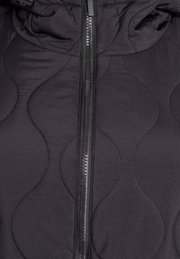 Juoda paminkštinta striukė su siuvinėta bangų rašto tekstūra, priekyje užtrauktuku ir gobtuvu. Medžiaga atrodo lygi su švelniu blizgesiu.