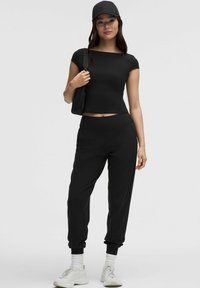Haut court noir et jogging noir en tissu doux, assortis d'une casquette noire et de baskets claires, offrant une coupe décontractée.