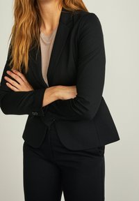 Schwarzer maßgeschneiderter Blazer mit taillierter Form und langen Ärmeln, gefertigt aus glattem Stoff, mit einer Zwei-Knopf-Verschluss und starken Schulternähten.