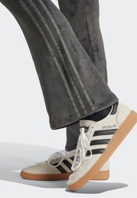 Adidas Spezial sneakers, featuring a beige suede upper, black stripes, and gum rubber sole. Gray ribbed pants with two vertical stripes.