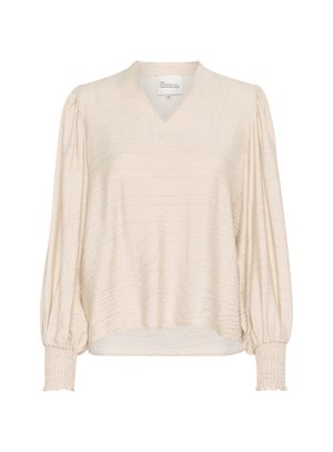 Blouse couleur crème avec un décolleté en V, des manches longues ballons et des poignets froncés. Présente un motif texturé pour plus de détails. Tissu doux et lisse.