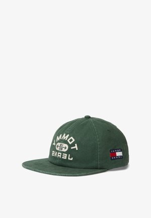 Žalia medvilninė kepurė su išlenktu snapeliu, ant kurios baltomis raidėmis parašyta „TOMMY JEANS“ ir yra logotipas, šone taip pat yra raudonos, baltos ir mėlynos spalvų vėliavos lopas.