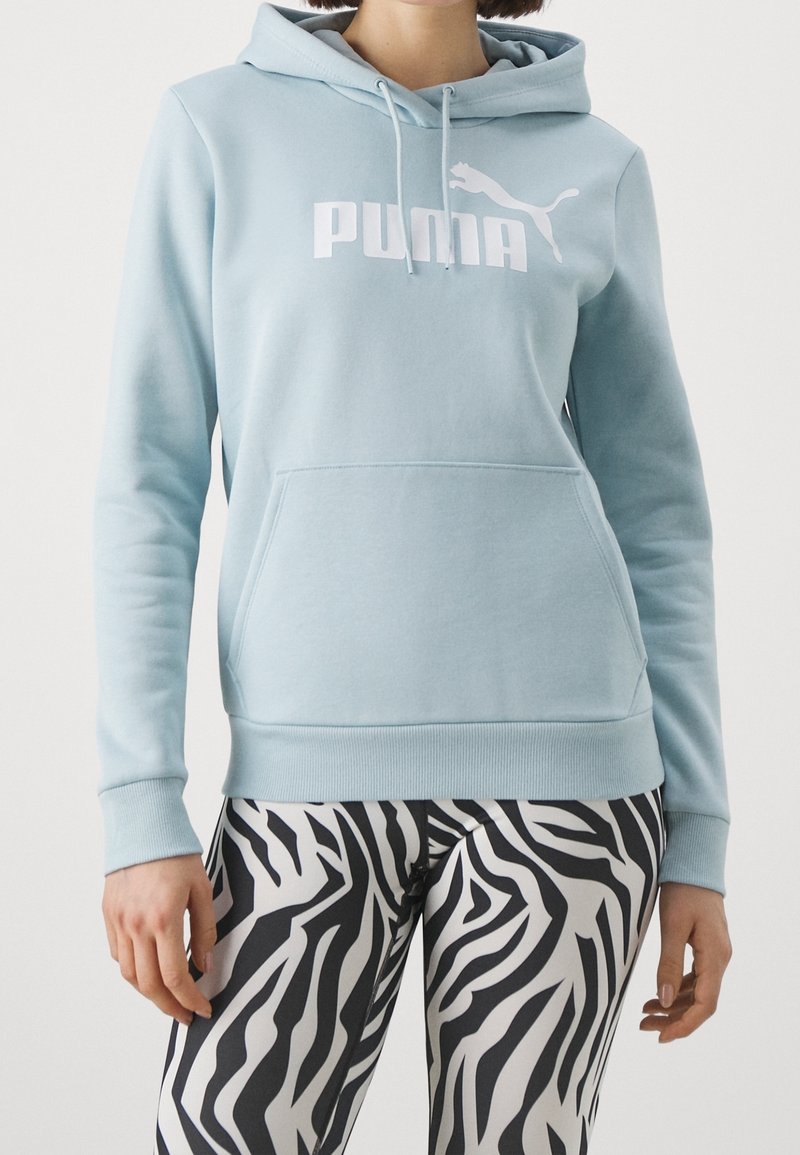 Felpa leggera blu con tasca a marsupio, presenta il logo bianco "PUMA" e una grafica di un gatto; abbinata a legging a stampa zebra in bianco e nero.