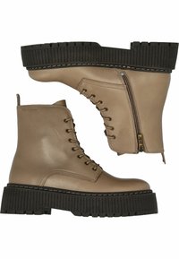 Botas de tobillo de cuero marrón claro con cordones en la parte frontal, cremallera lateral y suela de plataforma de goma negra con acanaladuras. Presenta detalles de costura y punta redondeada.