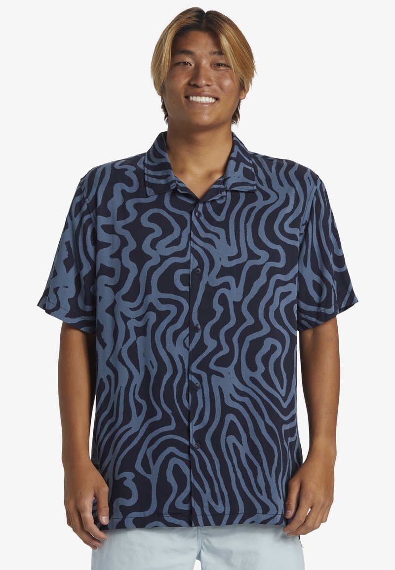 Camicetta a maniche corte con bottoni di colore blu navy con un motivo ondulato azzurro chiaro. Realizzata in un tessuto leggero con una vestibilità comoda.