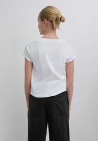 Tricou alb cu mâneci scurte, decolteu rotund, croială lejeră și tivuri suflecate, asortat cu pantaloni negri cu talie înaltă, având două buzunare în spate.