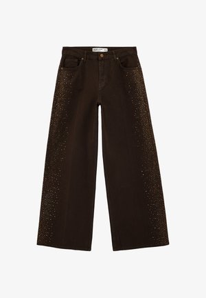 Vaqueros de pierna ancha en marrón oscuro con adornos de tachuelas doradas a lo largo de los lados exteriores y diseño clásico de cinco bolsillos.