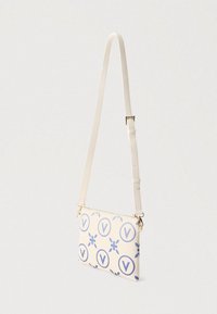 Kremfarvet crossbodytaske med justerbar rem, dekoreret med blå cirkel- og blomstermønstre, hængende mod en ensartet lys baggrund.