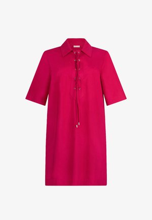 Robe rose vif arrivant aux genoux, avec manches courtes, col pointu, et détail à l'avant avec lacets, œillets métalliques et extrémités à pompons.