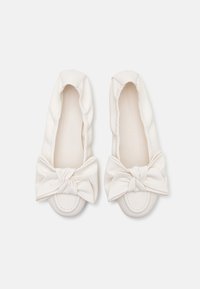 Chaussures plates blanches et douces avec bouts arrondis et grands nœuds décoratifs à l'avant, vues de dessus sur un fond uni.
