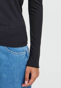 Black ribbed long-sleeve top with a fitted design, paired with light blue denim jeans featuring a side pocket and visible stitching accents.
