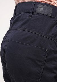 Granatowe spodnie cargo z teksturowanej bawełny, z tylnymi kieszeniami i naszywką z logo przy pasku.