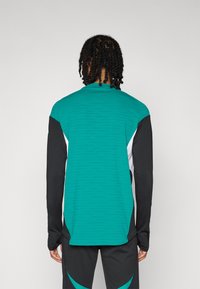 Jūros žydrumo sportinė palaidinė su juodomis ilgomis rankovėmis. Turi tekstūruotą paviršių ir aukštą kaklo dizainą. Paprasta nugara su kontrastingais skydelių akcentais.