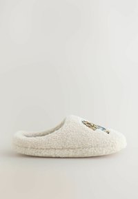 Krämfärgad toffel tillverkad av fluffigt, texturerat material med en broderad björndesign på ovansidan. Sluten bakdel, lätt att ta på.