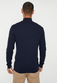 Donkerblauwe gebreide trui met hoge kraag, slim fit en geribbelde manchetten. Soepele textuur, minimalistisch ontwerp, ideaal om te laagjes te dragen.