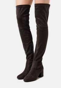 Stivali in suede marrone al ginocchio con tacco a blocco, caratterizzati da una texture liscia, cerniera laterale e dettagli cuciti lungo il bordo superiore.