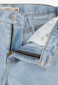 I jeans in denim azzurro chiaro presentano una cerniera dorata e una chiusura a bottone color bronzo. Inclusa una etichetta bianca e dettagli di cucitura lungo il cinturino.