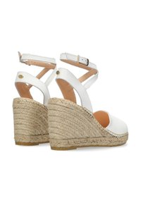 Witte leren instappers met straps en een geweven jute hak en rubberen zool. Voorzien van een verstelbare enkelband en een minimalistisch ontwerp.